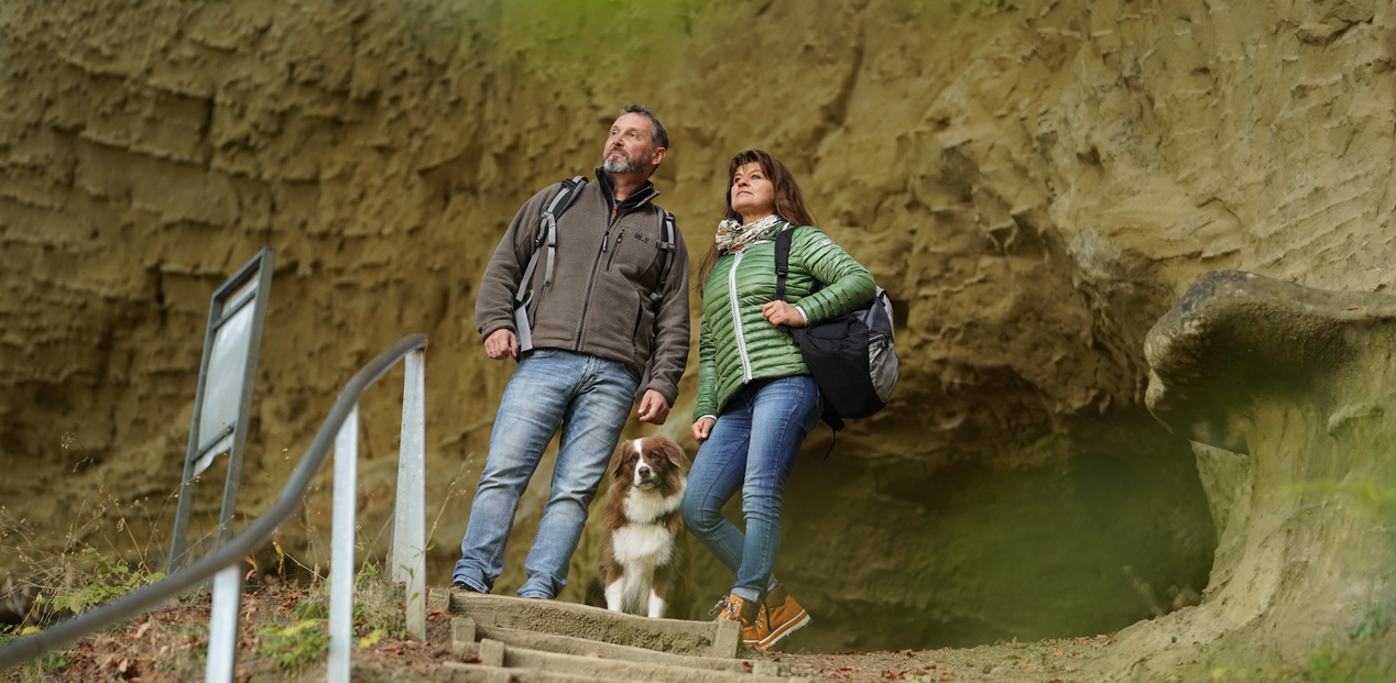 Paar steht mit Hund an der Treppe zu den Heidenhöhlen
