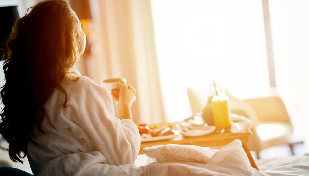 Frau sitzt mit Bademantel bekleidet auf einem Bett in einem Hotel